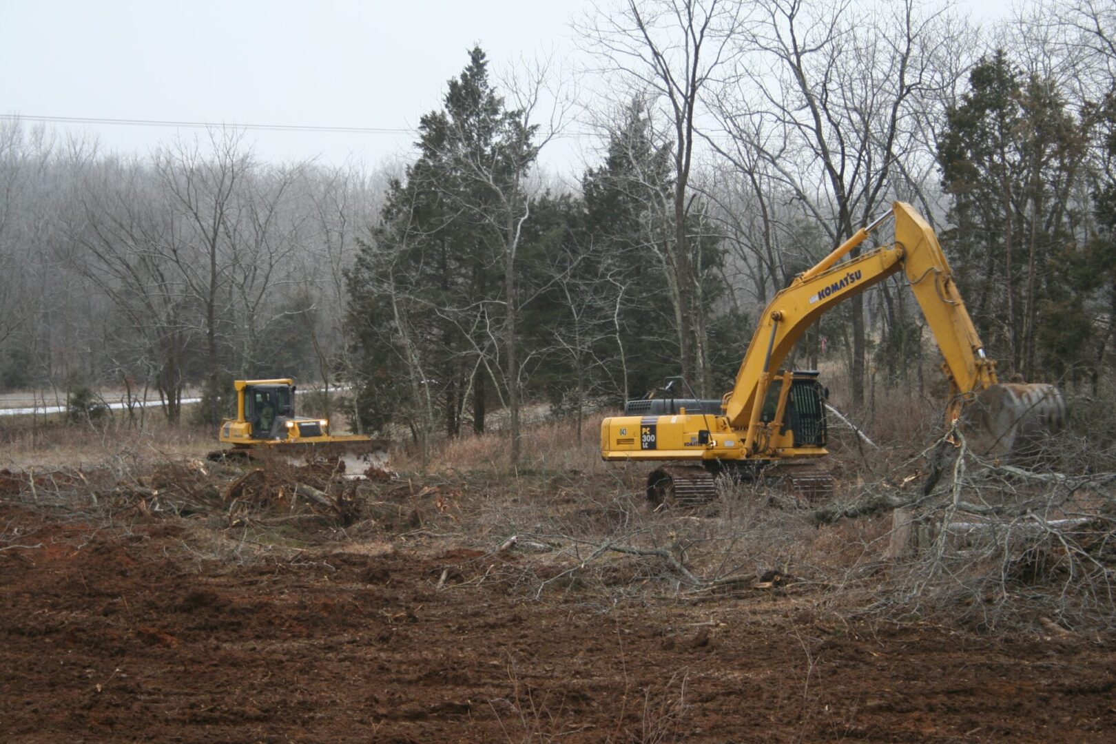 Land clearing operation with an excavator and a bulldozer in a forested area.