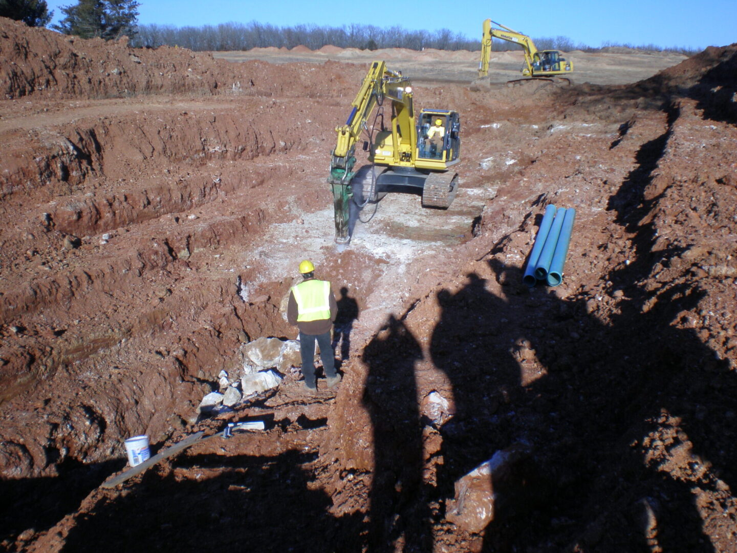 Construction workers and excavators at a large excavation site with pipes ready for installation.