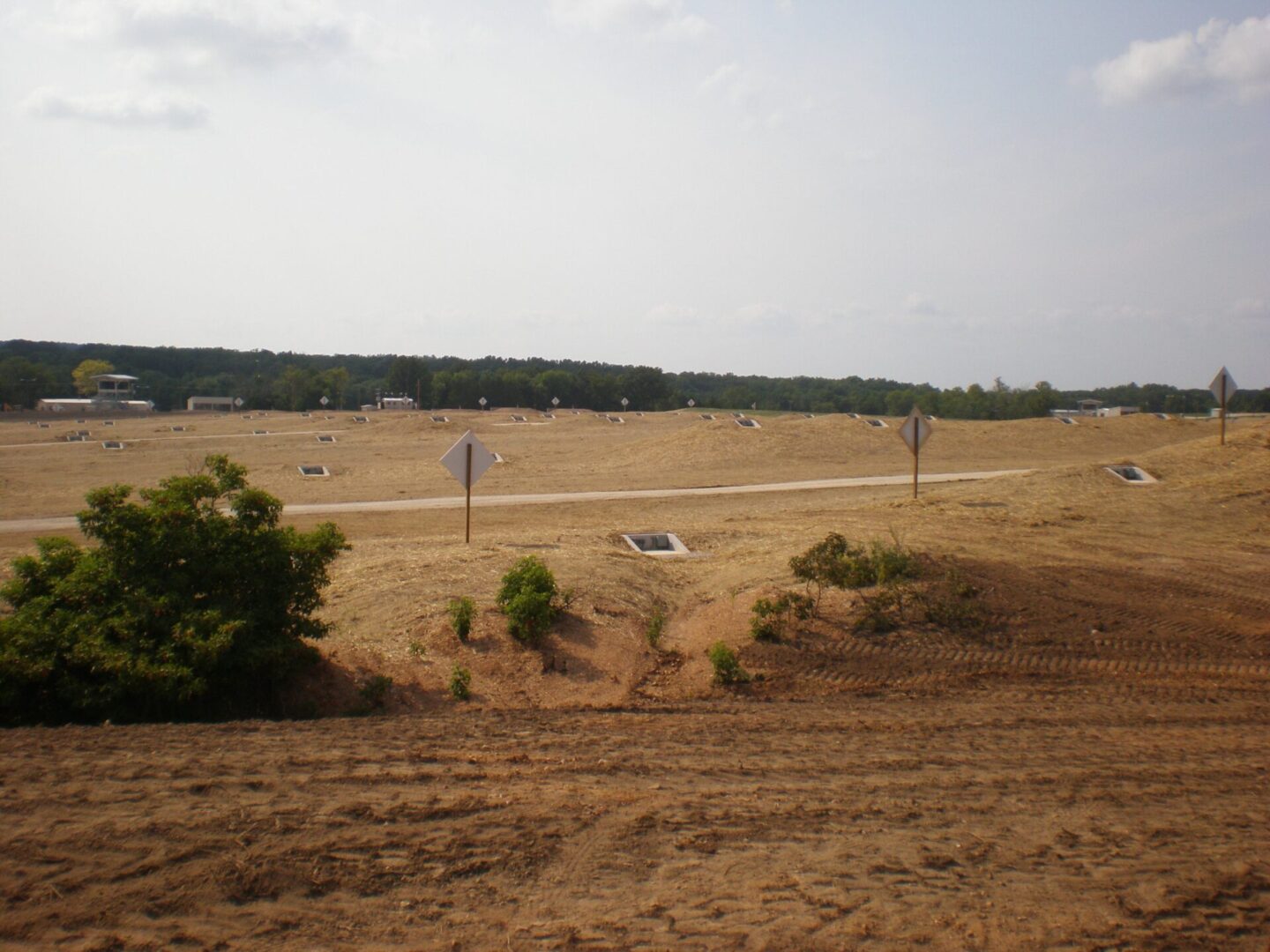 A newly constructed road intersection with yield signs, surrounded by a cleared and undeveloped area with a few scattered trees in the background.