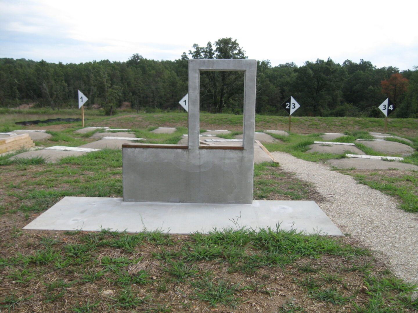 Concrete shooting range stations with numbered signs in a grassy outdoor area.