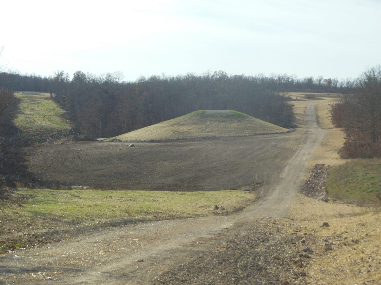 A dirt road winding towards a grassy hill in a barren landscape.